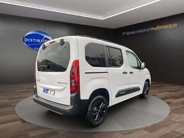 Vue 3/4 arrière droite d'un Citroën Berlingo blanc 2025 avec vitres teintées et jantes noires en showroom.