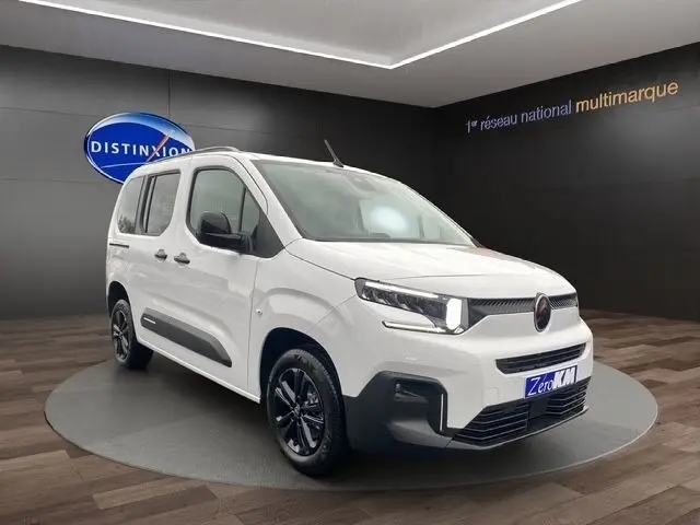 Vue 3/4 avant d'un Citroën Berlingo blanc 2025 avec jantes noires et calandre moderne en showroom.
