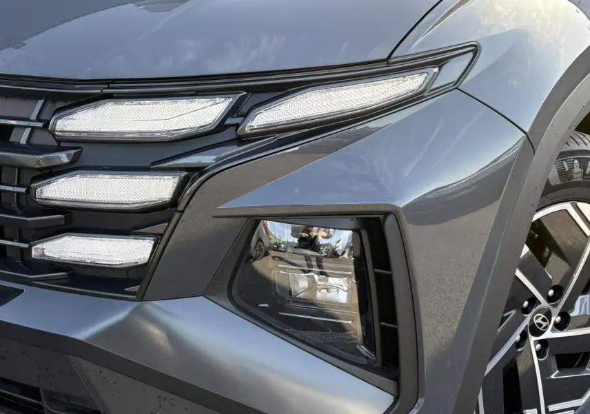 Gros plan sur le phare avant droit et la calandre du Hyundai Tucson 2025 en Ecotronic Gray métallisé.