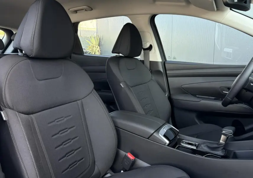 Intérieur du Hyundai Tucson 2025 vu côté passager, sièges noirs en tissu avec console centrale et levier de vitesses.