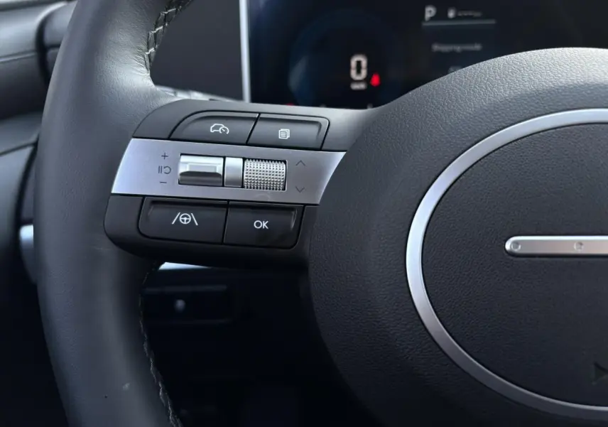 Gros plan sur les commandes gauche du volant cuir du Hyundai Tucson 2025, avec tableau de bord numérique en arrière-plan.