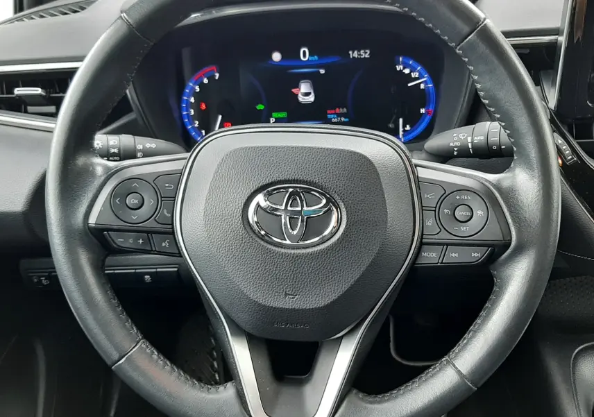 Vue rapprochée du volant en cuir noir d'une Toyota Corolla 122 CH Dynamic 2022 avec tableau de bord digital éclairé.