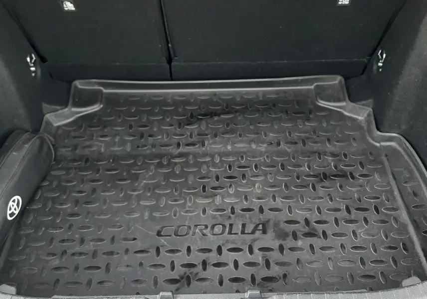 Coffre ouvert d'une Toyota Corolla blanche 2022, vue de dessus montrant le tapis de coffre noir marqué "COROLLA".