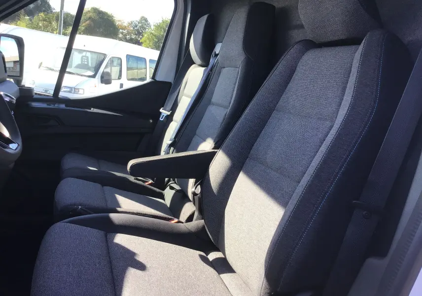 Vue intérieure côté passager du Renault Master 2025 avec sièges gris et accoudoir, banquette et rangement visibles.
