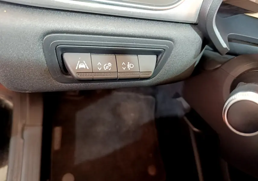 Gros plan sur les boutons de réglage d'assistance et phares du tableau de bord du Renault Captur Business noir de 2020.