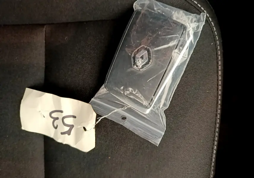 Clé Renault noire sous plastique sur siège tissu noir, vue rapprochée en plongée.