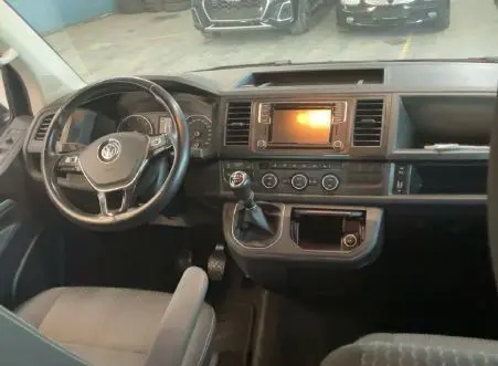 Vue intérieure du tableau de bord noir du Volkswagen Multivan T6 PH.1, avec volant, écran central et levier de vitesses manuel.