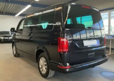 Vue 3/4 arrière droite d’un Volkswagen Multivan T6 noir, avec vitres teintées et feux arrière rouges, en intérieur.
