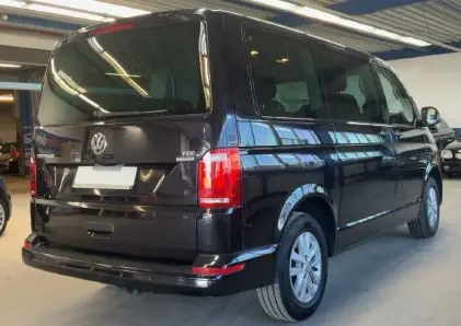 Vue 3/4 arrière droite d’un Volkswagen Multivan T6 noir, version Trendline 2015, avec feux arrière rouges et vitres teintées.