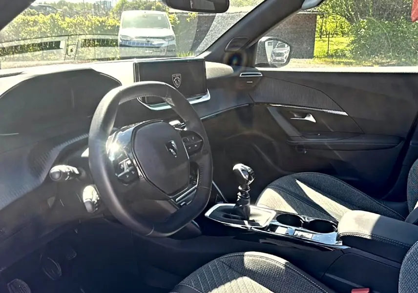 Vue intérieure côté conducteur du Peugeot 2008 2025, montrant le volant compact, la boîte manuelle et les sièges en tissu gris.