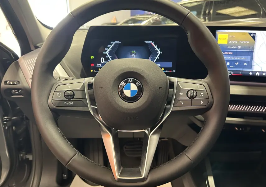 Vue rapprochée du volant cuir noir BMW avec commandes intégrées et tableau de bord numérique lumineux.