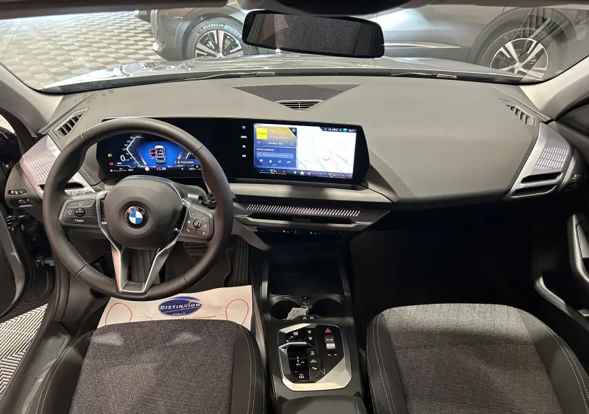 Intérieur BMW Série 1 120DA 2024, vue du poste de conduite avec tableau de bord numérique et écran central tactile.
