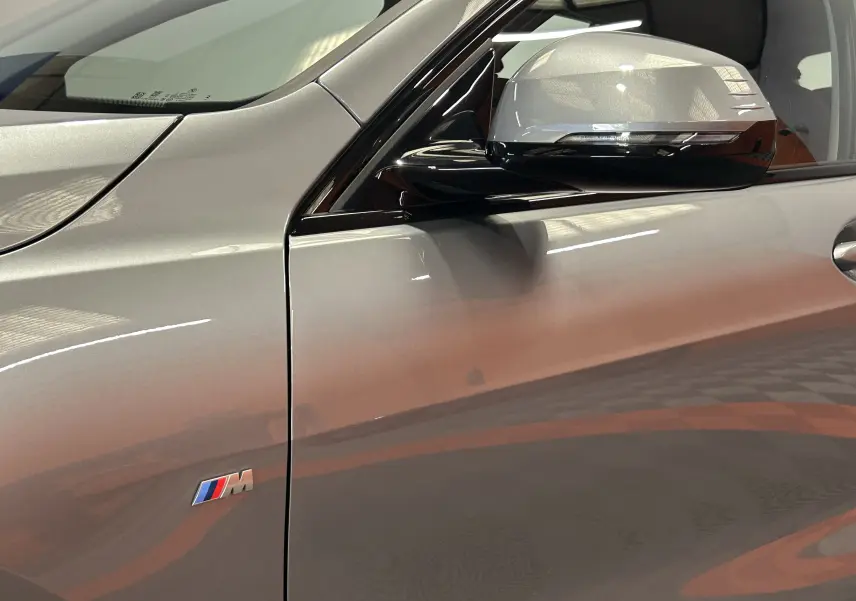 Gros plan sur le côté gauche gris Skyscrap de la BMW Série 1 120DA M Sport avec logo M et rétroviseur bicolore.