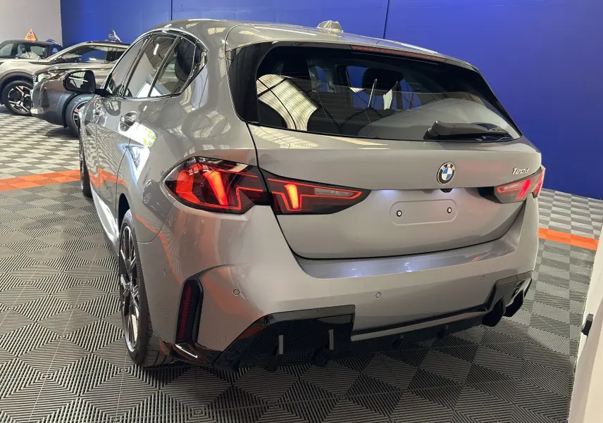 Vue 3/4 arrière droite d'une BMW Série 1 120DA M Sport gris Skyscrap avec feux LED allumés en intérieur showroom.