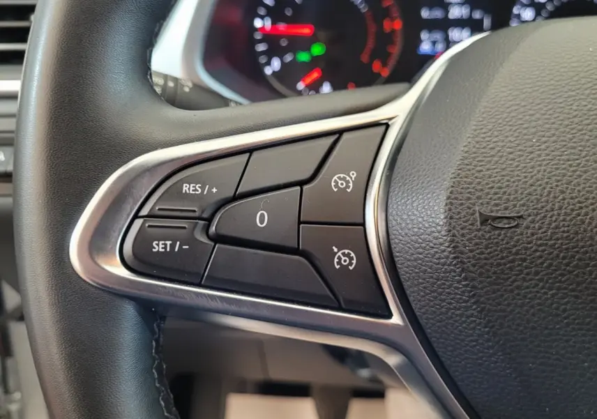 Gros plan sur les commandes au volant gauche du Renault Captur Business gris clair, avec tableau de bord lumineux en arrière-plan.