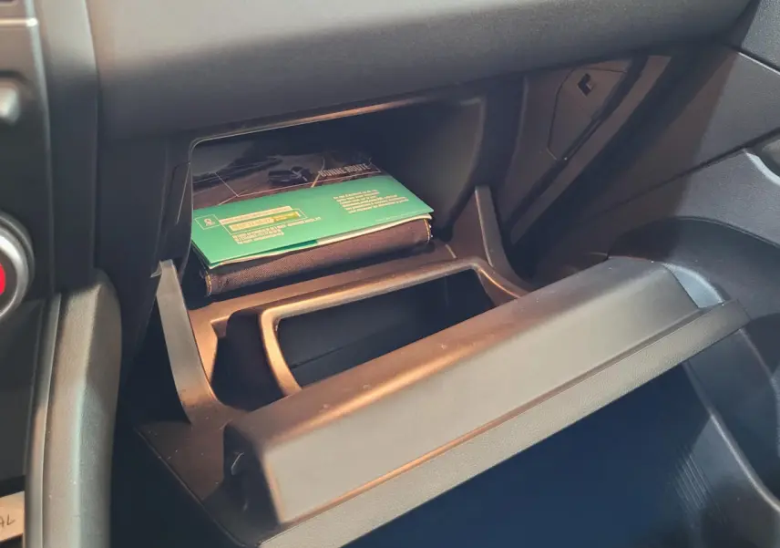 Gros plan sur la boîte à gants ouverte du Renault Captur Business gris clair, montrant un manuel et un espace de rangement intérieur.