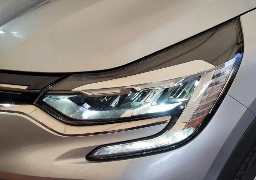 Gros plan sur le phare avant droit allumé d'un Renault Captur gris clair 2021, soulignant ses LED modernes.