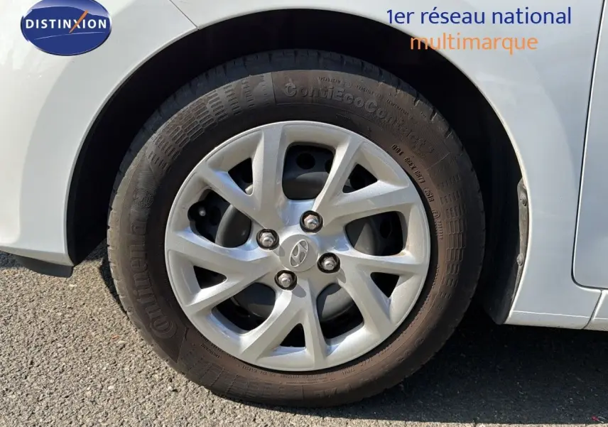 Gros plan sur la roue avant droite d'une Hyundai i10 blanche de 2018 avec jante argentée et logo Hyundai visible.