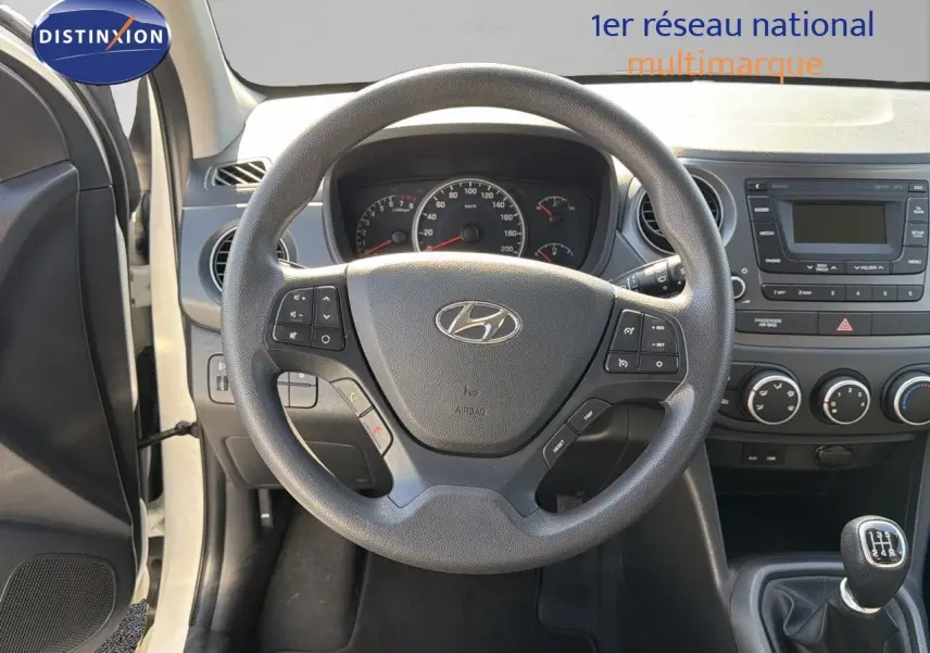 Vue centrée sur le volant Hyundai i10 blanche 2018 avec tableau de bord et levier de vitesses manuel visible.