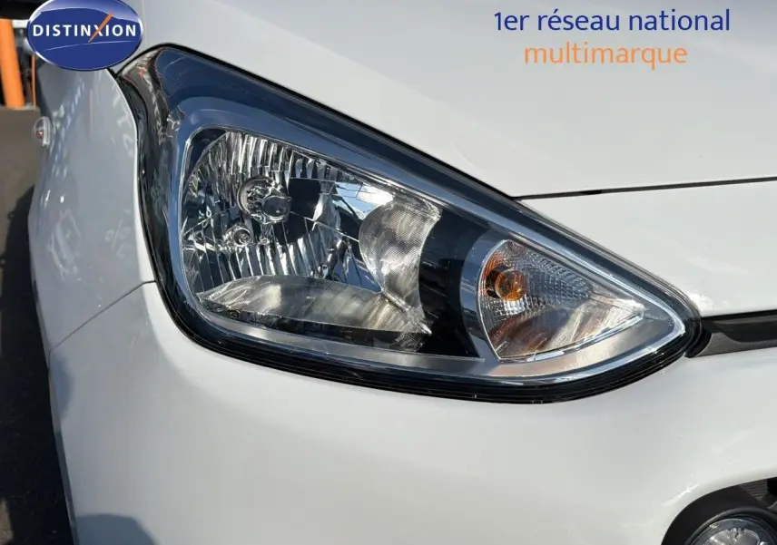 Gros plan sur le phare avant droit d'une Hyundai i10 blanche de 2018, soulignant les détails du bloc optique.