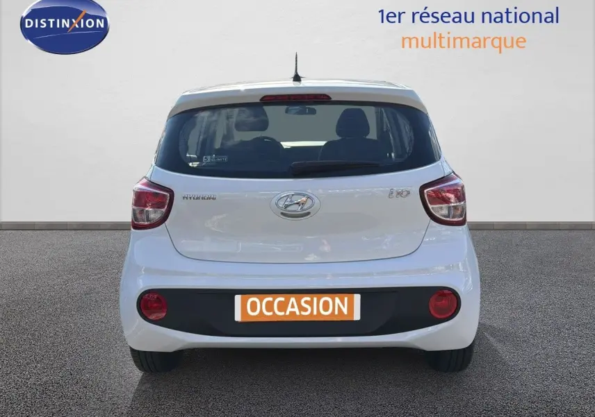 Vue arrière d'une Hyundai i10 blanche 2018 avec feux rouges et plaque d'occasion visible sur un sol gris.