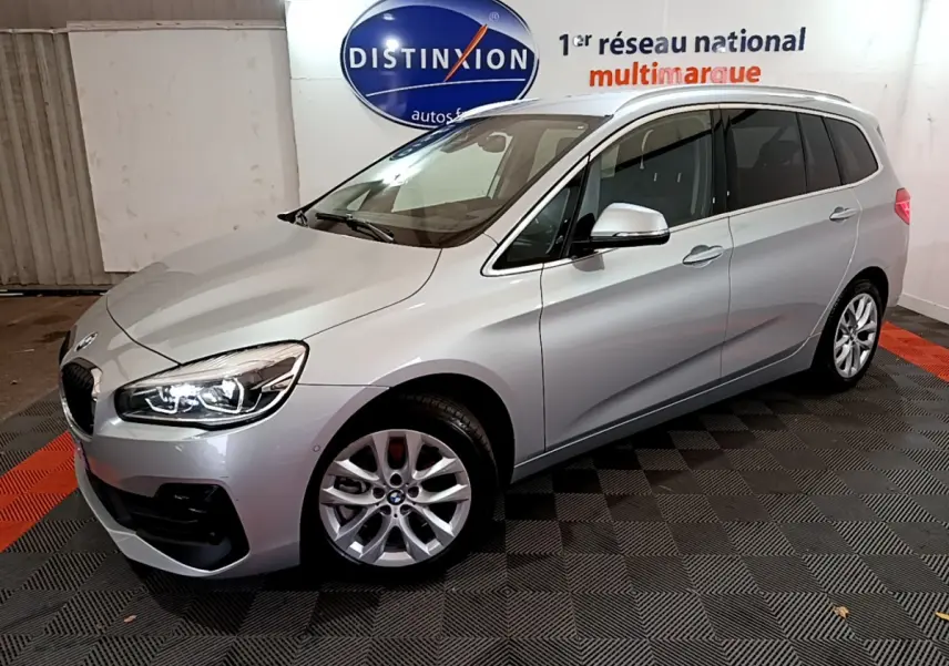 BMW Série 2 Gran Tourer 218d gris clair vue 3/4 avant droit avec phares LED allumés en intérieur showroom.