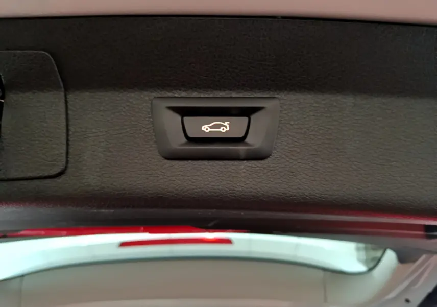 Gros plan sur le bouton d'ouverture électrique du coffre, situé sous le hayon du BMW Série 2 Gran Tourer gris clair.