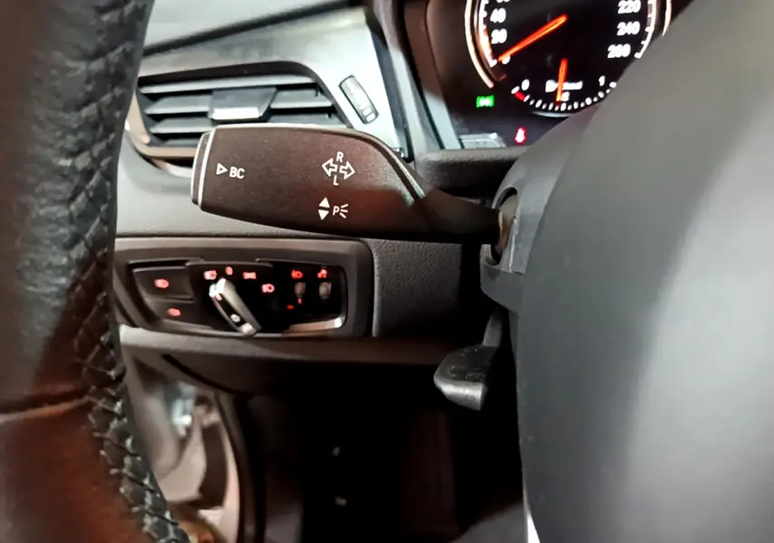 Gros plan sur la manette de clignotants et commandes d’éclairage du tableau de bord d’une BMW Série 2 Gran Tourer gris clair.