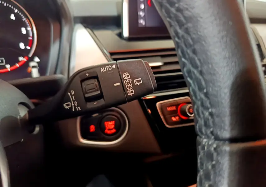 Détail intérieur du volant cuir noir de la BMW Série 2 Gran Tourer 218d, avec commande essuie-glace et bouton start/stop rouge.