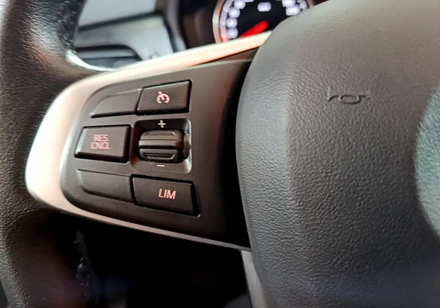 Gros plan sur les commandes du volant à gauche d'une BMW Série 2 Gran Tourer gris clair, boutons de régulateur de vitesse visibles.