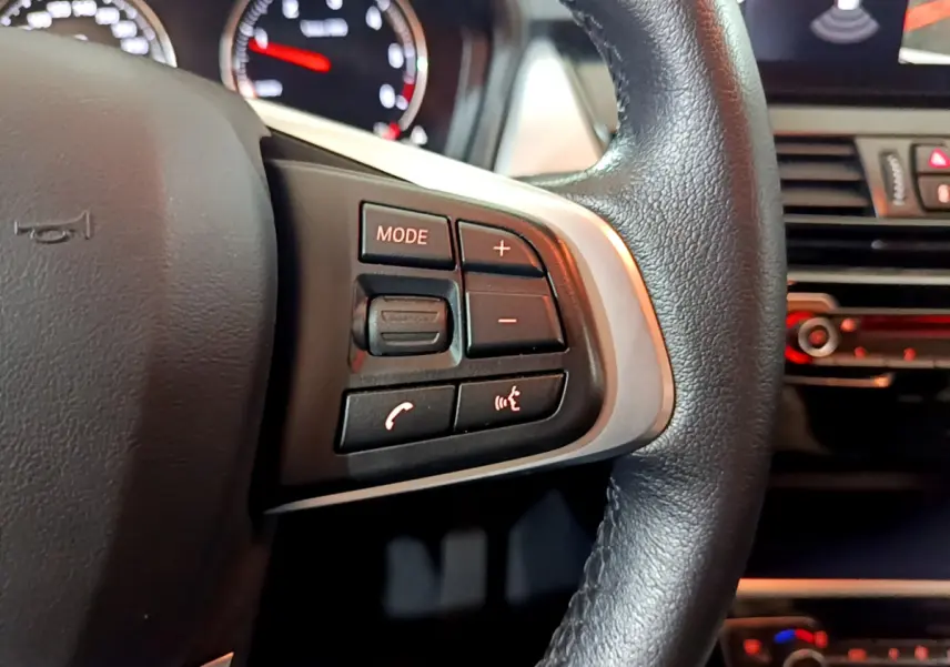 Gros plan sur la partie gauche du volant cuir noir d’une BMW Série 2 Gran Tourer 218d avec commandes multimédias.