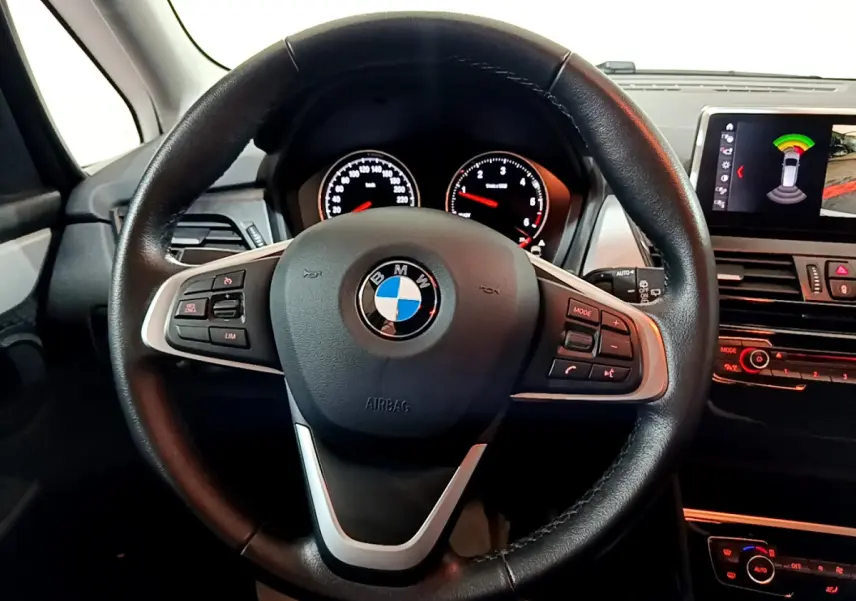 Vue intérieure centrée sur le volant cuir noir de la BMW Série 2 Gran Tourer 218d avec tableau de bord et écran multimédia.