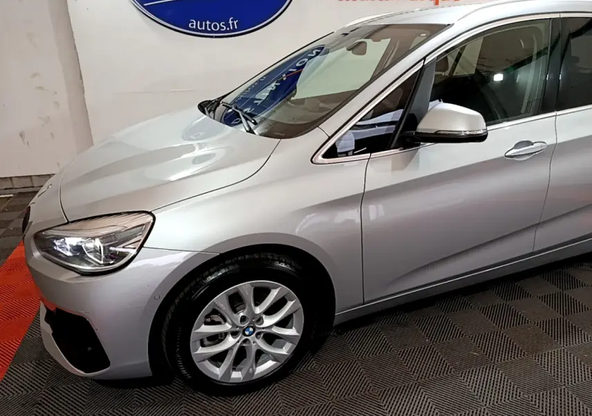 Vue 3/4 avant gauche d'une BMW Série 2 Gran Tourer 218d Lounge gris clair avec jantes alliage et rétroviseur argenté.