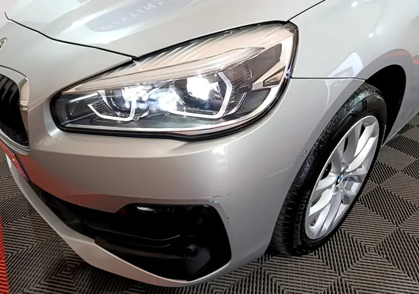 Gros plan sur l'avant droit gris clair de la BMW Série 2 Gran Tourer avec phare LED allumé et jante alu visible.