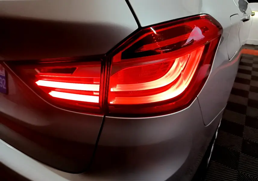Gros plan sur le feu arrière droit rouge allumé d'une BMW Série 2 Gran Tourer F46 gris clair, vue arrière latérale.