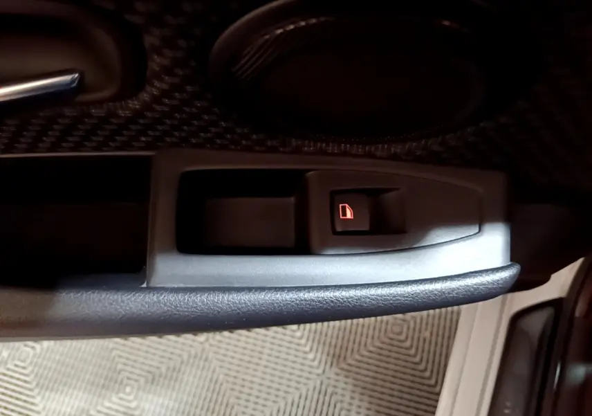 Gros plan sur le bouton de verrouillage de porte intérieur côté conducteur d'une BMW Série 2 Gran Tourer gris clair.