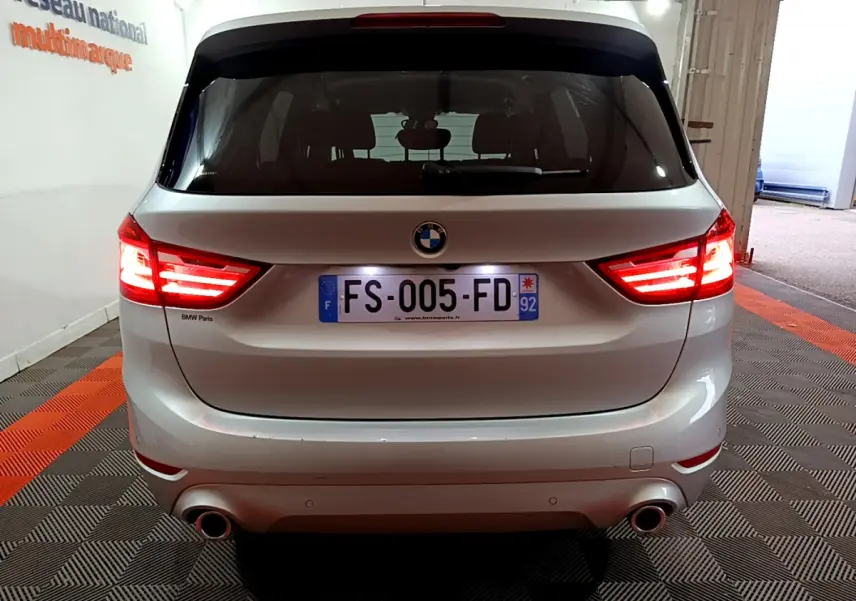 Vue arrière d'une BMW Série 2 Gran Tourer 218d Lounge gris clair avec feux LED allumés dans un garage.