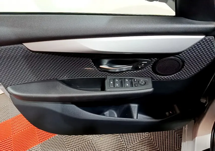 Gros plan sur la porte avant gauche de la BMW Série 2 Gran Tourer gris clair, avec commandes de vitres et haut-parleur intégré.