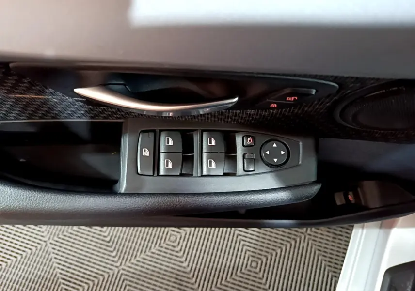 Gros plan sur les commandes des vitres et la poignée intérieure côté gauche d'une BMW Série 2 Gran Tourer gris clair.