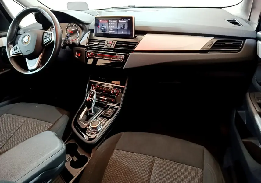 Vue intérieure avant de la BMW Série 2 Gran Tourer 218d Lounge, tableau de bord noir avec écran central et volant cuir.