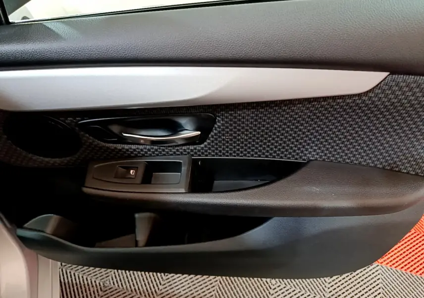 Gros plan sur la porte côté conducteur de la BMW Série 2 Gran Tourer gris clair, avec poignée alu et habillage tissu à motifs.