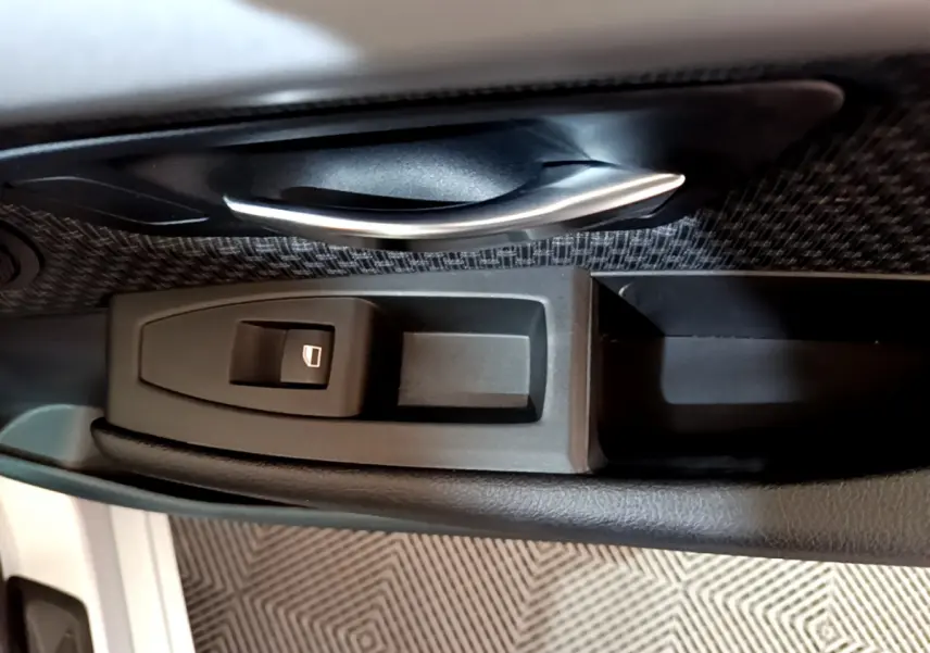 Gros plan sur la poignée intérieure et le bouton de lève-vitre côté conducteur d'une BMW Série 2 Gran Tourer gris clair.