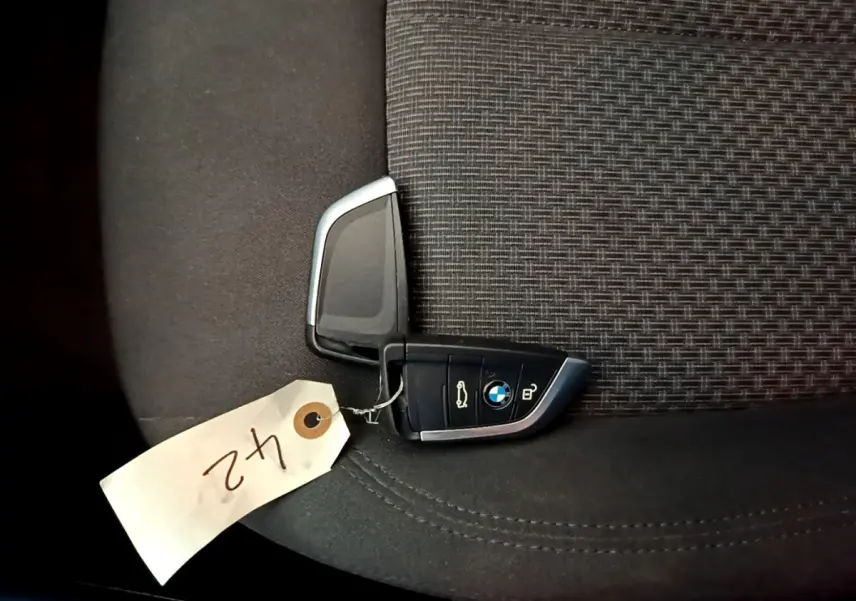 Clé BMW posée sur un siège tissu gris foncé à motifs, avec étiquette blanche numérotée "42".