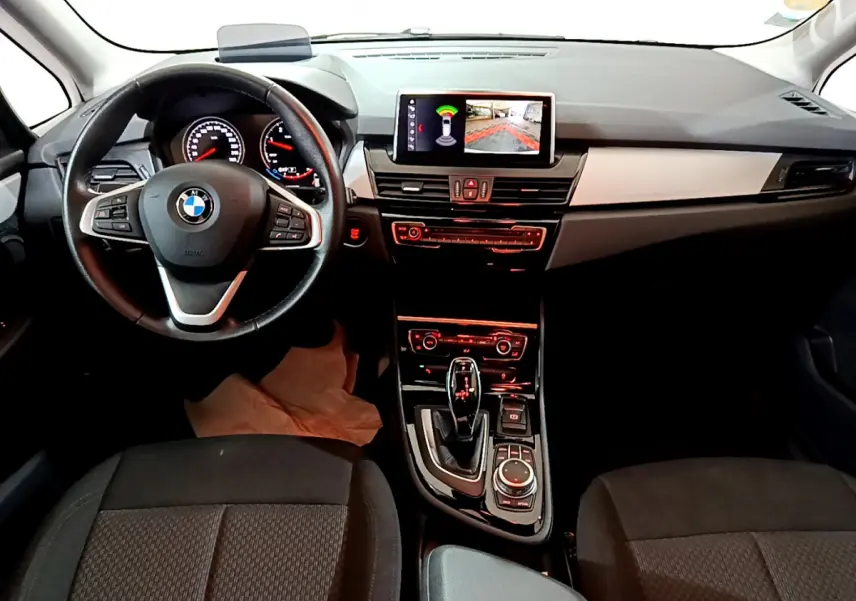 Vue intérieure avant de la BMW Série 2 Gran Tourer 218d Lounge, tableau de bord et volant cuir noir avec écran central.