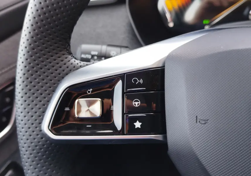 Gros plan sur les commandes multifonctions à gauche du volant perforé du MG MOTOR ZS hybride, finition noire et argentée.
