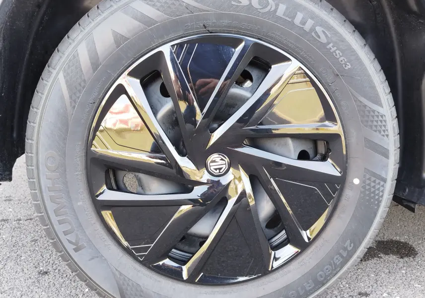 Gros plan sur la jante noire brillante à design géométrique du MG MOTOR ZS 1.5L HYBRID+ 2026, pneu Kumho visible.