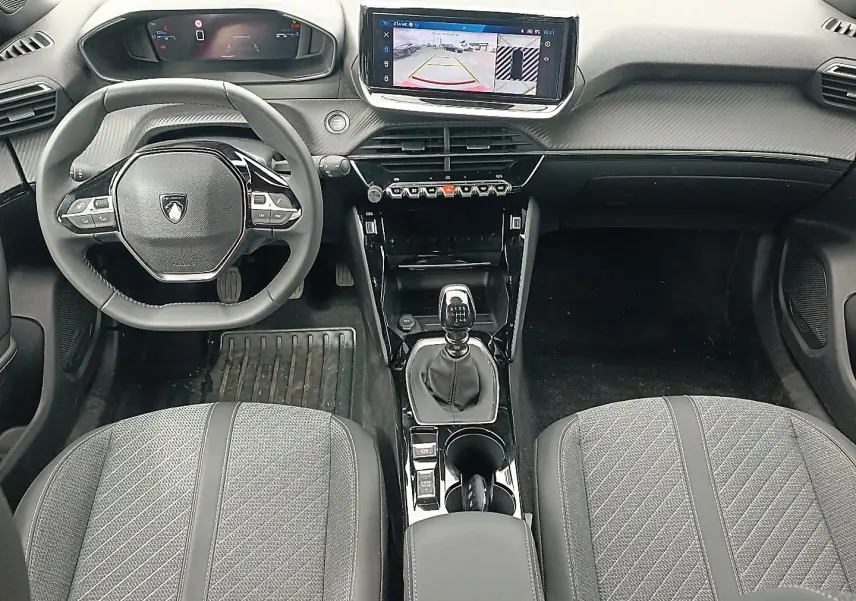 Vue intérieure avant du Peugeot 2008 1.2 100 allure 2025, volant multifonction, écran tactile et levier de vitesse manuel.