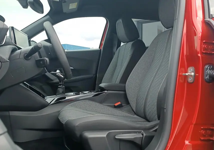 Vue intérieure côté conducteur de la Peugeot 2008 rouge elixir, montrant les sièges en tissu gris et la console centrale.