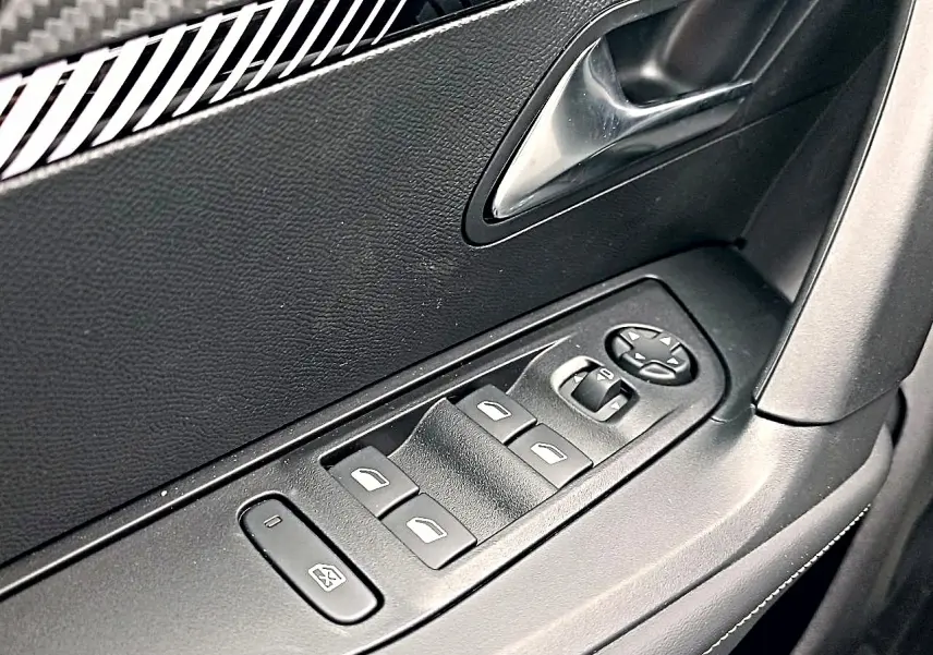Gros plan sur la commande des vitres électriques côté conducteur de la Peugeot 2008 rouge Elixir, avec poignée intérieure noire.