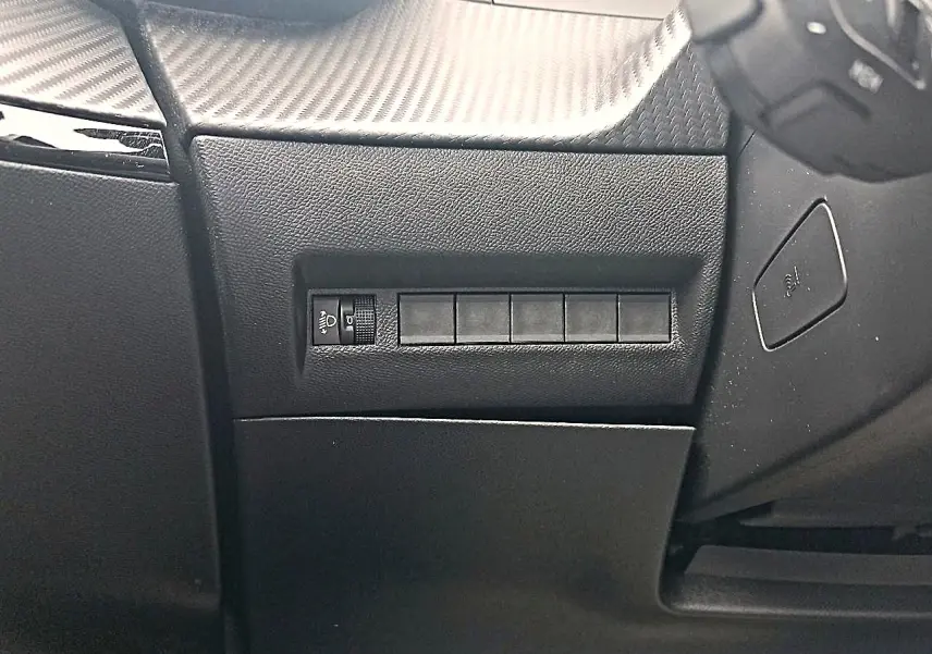 Détail intérieur côté gauche du tableau de bord noir avec commande de réglage des phares sur Peugeot 2008 rouge Elixir.